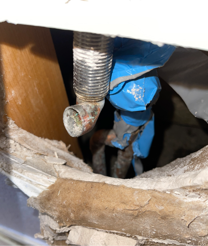 Bottom of spigot with threads and end of copper pipe attached. There is a noticeable twist in the pipe. Behind that is the original copper water pipe wrapped in blue tape. This is all inside a hole in the drywall. 